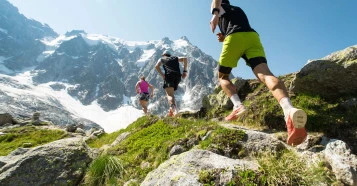 low angle view of three people running across rocks towards a snow-covered mountain