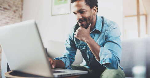 man wearing casual clothes sitting on sofa looking at laptop