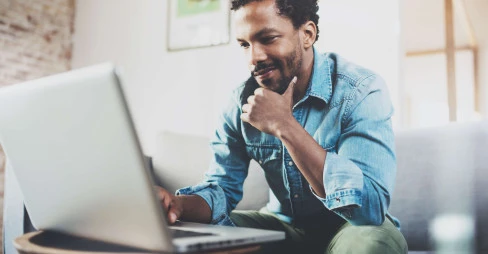 man wearing casual clothes sitting on sofa looking at laptop