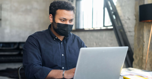 man in an office on a laptop while holding mobile phone