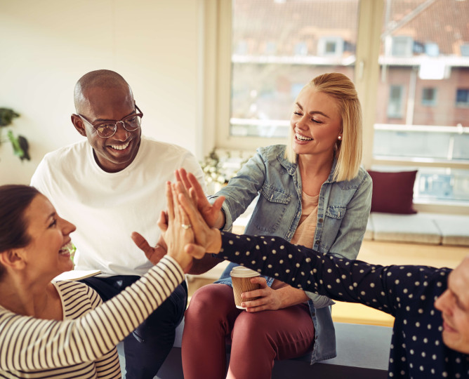 eye level view of four people high-fiving in a casual working environment