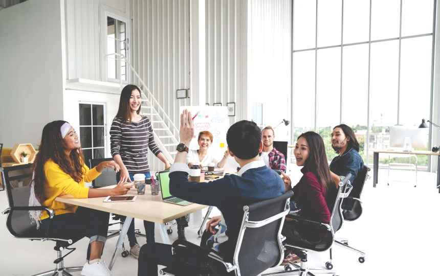 seven people smiling at meeting table with a man's arm raised