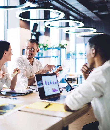 four people in smart clothing sitting in a office communal area with laptops and documents