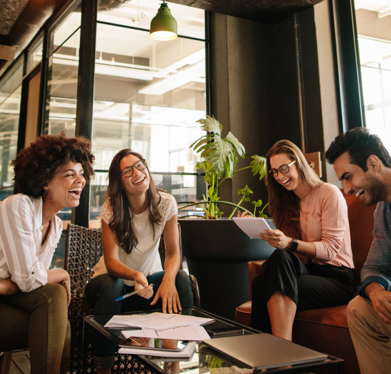 A froup of four colleague in an office setting. They are gather around a table covered with work-related documents. 
