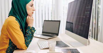 woman in hijab analysing data on apple mac with laptop and notes on the desk
