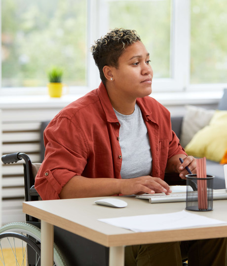 woman in a wheelchair wearing casual clothes working at a desk at home