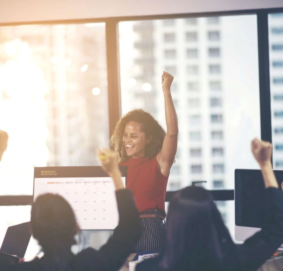 woman in an office punching the air with onlookers celebrating 