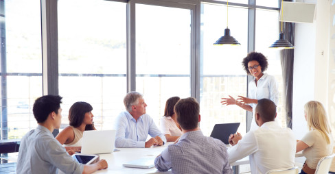 woman leading meeting with seven other people sitting at a table