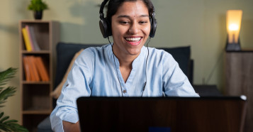 woman in blue shirt smiling at laptop wearing a headset